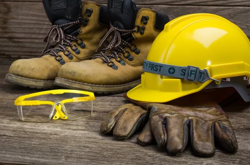 Botas, luvas, óculos de proteção e capacete amarelo sobre uma bancada