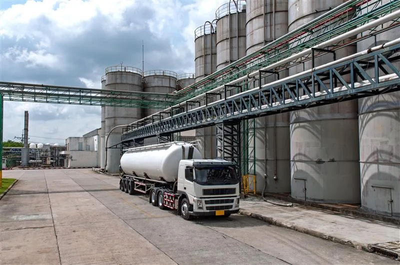 Caminhão-tanque estacionado em frente a tanques de armazenamento de combustíveis em uma indústria petroquímica, representando o ambiente de atuação de profissionais que necessitam do Curso NR-20 para operar com segurança.
